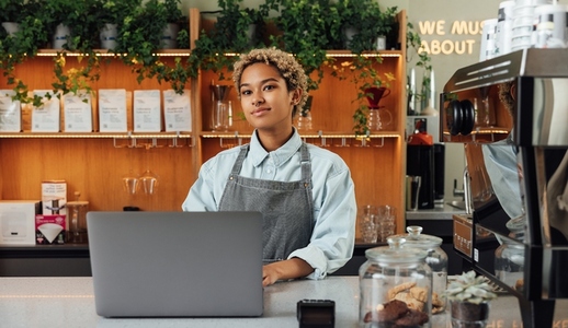 Young female coffee shop owner at counter with a laptop  Woman barista in an apron working in a coffee shop