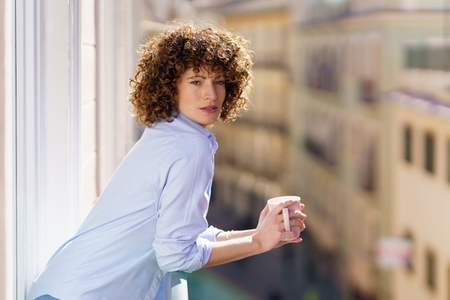 Curly haired woman drinking coffee on balcony