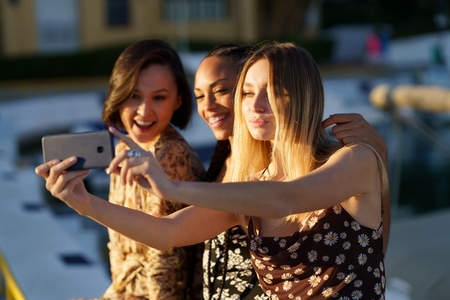 Joyful multiracial women taking selfie on wharf
