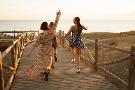 Relaxed diverse women joyfully running on boardwalk on seashore