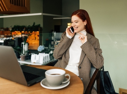 Cheerful redhead female making a call while sitting in a coffee shop
