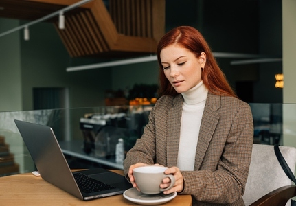 Young female entrepreneur in a cafe in morning  Woman with ginger hair working from a coffee shop