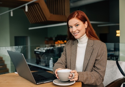 Beautiful businesswoman with ginger hair looking at camera while holding a cup