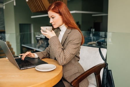 Businesswoman in formal wear typing on laptop in cafe  Young female drinks coffee and work remotely