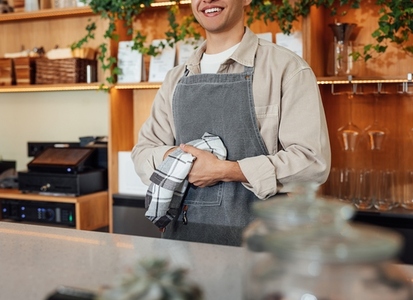 Cropped of an unrecognizable bartender in apron wiping his hands with towel while standing at bar counter