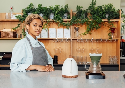 Young woman in apron working as a barista standing at the counter with a kettle  filter and scales