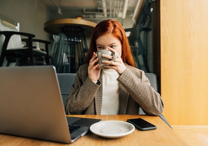 Woman drinking coffee and looking at laptop while sitting at a table in cafe