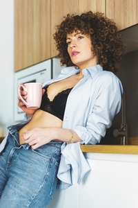 Adult woman with unbuttoned shirt drinking coffee in kitchen