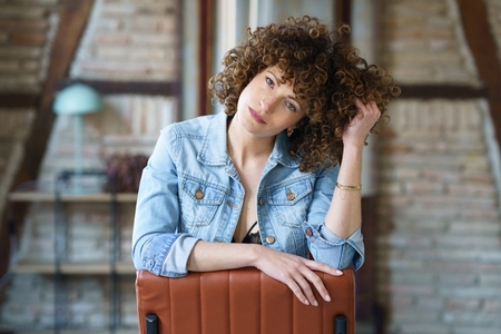 Pensive woman sitting on chair and touching curly hair