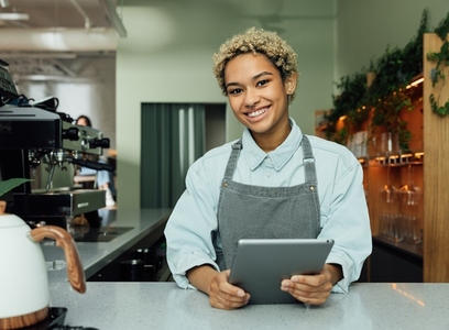 Smiling female barista with digital tablet in the cafe  Portrait of a young female in an apron at a counter in a coffee shop