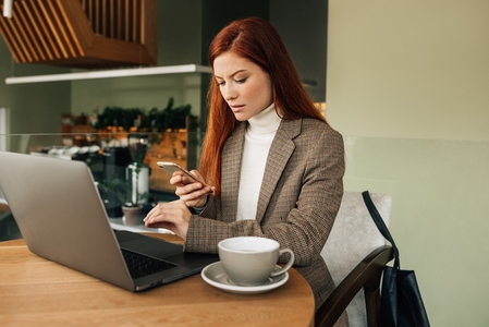 Woman with ginger hair holding a smartphone sitting at a cafe  Businesswoman working from the coffee shop