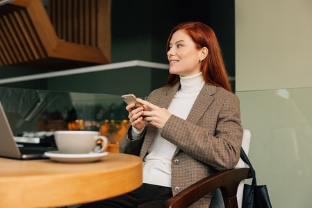 Businesswoman with ginger hair sitting in a cafe and using a smartphone
