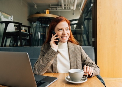 Smiling redhead female in formal attire working remotely from the cafe