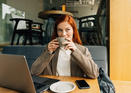 Businesswoman in a jacket holding a cup sitting at cafe in the morning