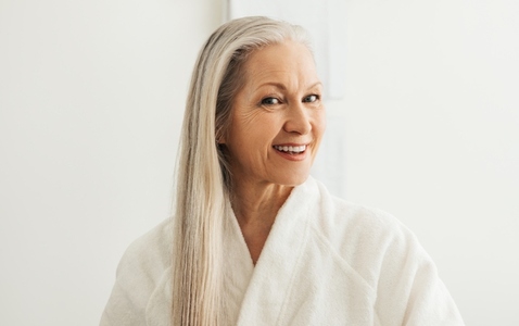 Cheerful female with gray hair in a bathrobe looking at her reflection