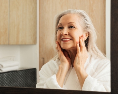 Aged woman with grey hair examines her face in bathroom in the morning