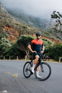Male cyclist in sports clothes standing with a road bike against a mountain with clouds
