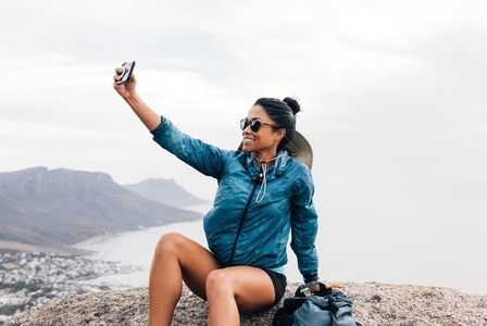 Cheerful woman taking a selfie on smartphone while taking a break during a hike