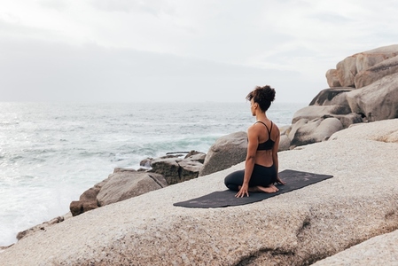 Slim woman in sports clothes sitting on a yoga mat and looking at the ocean