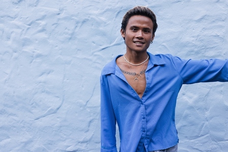 Smiling stylish guy in a blue shirt posing against a blue wall
