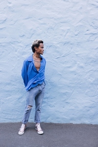 Full length of a young guy in a blue shirt standing at the wall and looking away