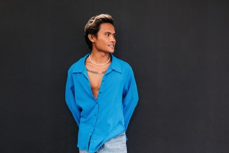 Young stylish guy in blue shirt posing at black wall