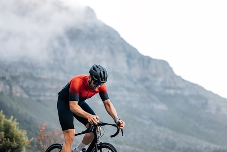 Professional rider on a bike doing intense training outdoors against the mountain with clouds