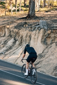 Back view of a male cyclist in black sports attire riding his bike up a hill on a country road