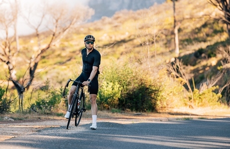 Male cyclist in black sportswear standing with bike on a road in wild terrain