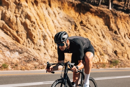 Tough cyclist on his road bike  Professional cyclist in black sport attire exercising in wild terrain