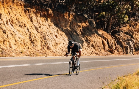Professional sportsman riding his bicycle on an empty road in wild terrain  Male cyclist practicing riding on bicycle