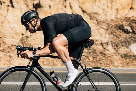 Professional cyclist in black sportswear riding road bike against the mountain  Muscular male doing intense training on bike outdoors