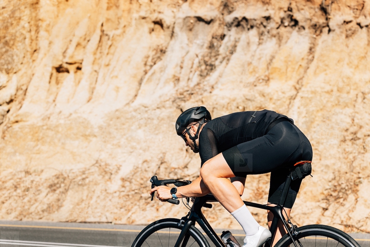 Triathlete riding road bike outdoors. Muscular cyclist in black sportswear