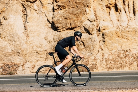 Side view of a young male cyclist riding his bicycle on a road while going up on a hill