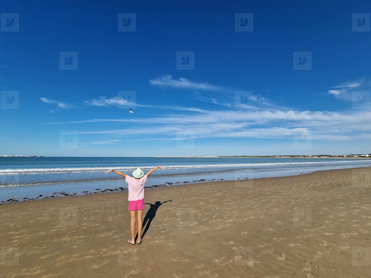Girl opening her arms in front of the sea with a seagull flying in front of her