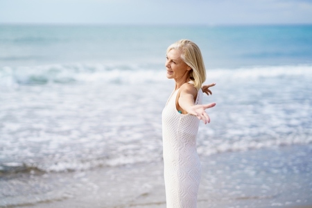 Mature woman opening her arms on the beach  spending her leisure time  enjoying her free time