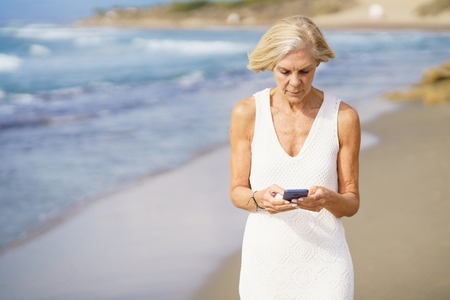 Senior woman using smartphone on beach in summer