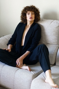 Stylish curly haired female sitting on sofa wearing black suit