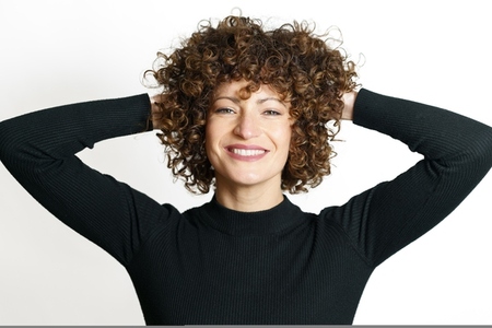 Happy woman with curly hair smiling with hands behind