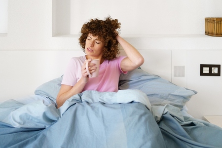 Sleepy female with cup of coffee in bedroom