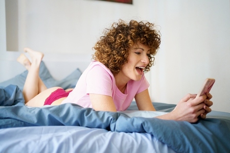 Happy woman using smartphone in bed at home