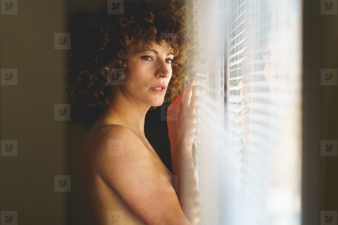 Sensual naked woman leaning on window