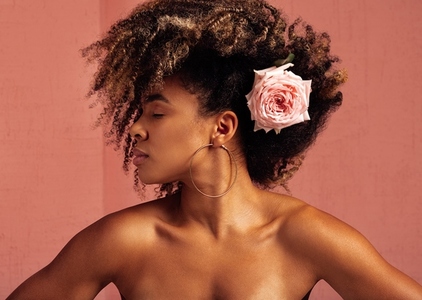 Woman with closed eyes against a pink background  Young female with flower in her curly hair