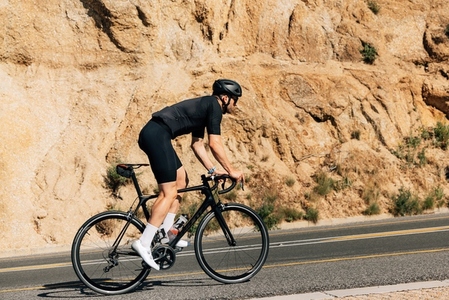 Cyclist in black sportswear doing intense training outdoors  Side view of a triathlete on a bicycle