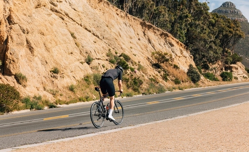 Rear view of a professional cyclist riding up on an empty road  Young male in cycling attire on a road bike