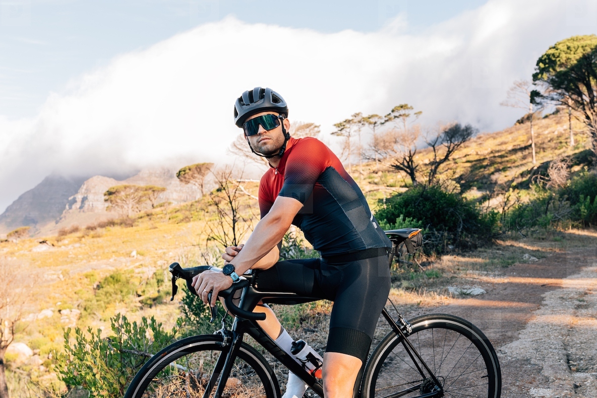 Portrait of a professional cyclist in helmet and glasses standing with bicycle against wild terrain