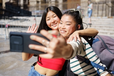 Delighted Asian women taking self portrait on smartphone and smiling during trip