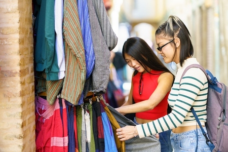 Female tourists choosing clothes in street market