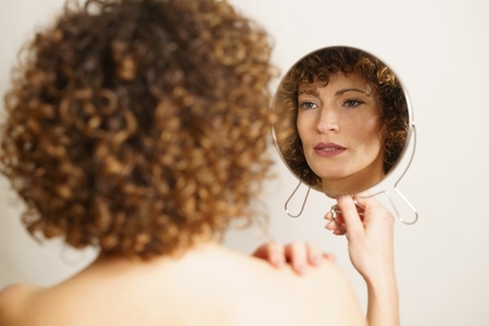 Charming adult female with makeup looking reflection in mirror