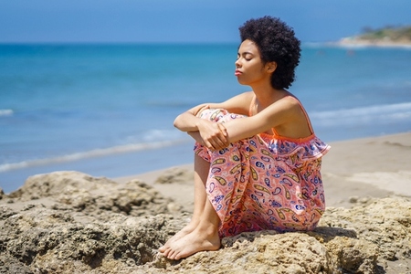 African American tourist sitting on stone and breathing fresh sea air